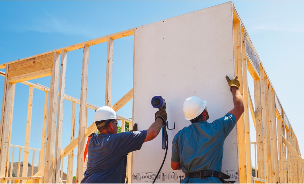 Workers attaching panels to a framed building, under a clear blue sky.