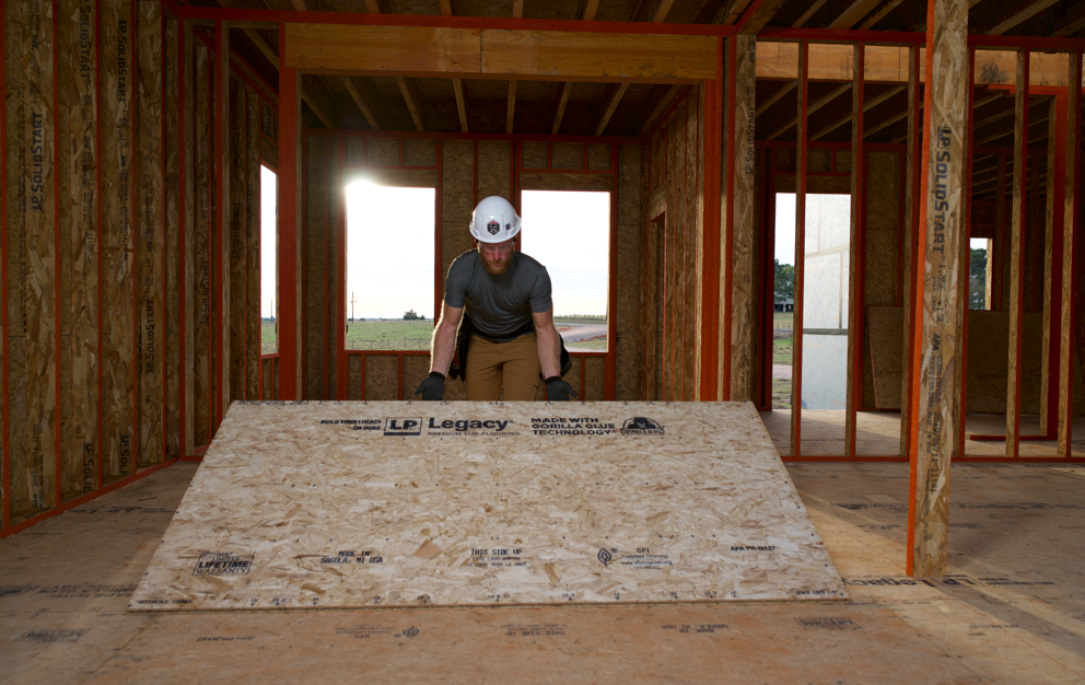 Worker placing a sheet of sub-flooring down in a new building under construction.