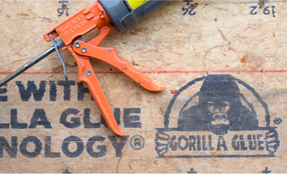 Gros plan du logo Gorilla Glue sur un panneau Legacy, avec un pistolet à calfeutrer posé dessus.