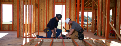 Deux ouvriers à l'intérieur d'un chantier martelant un support de revêtement de sol.