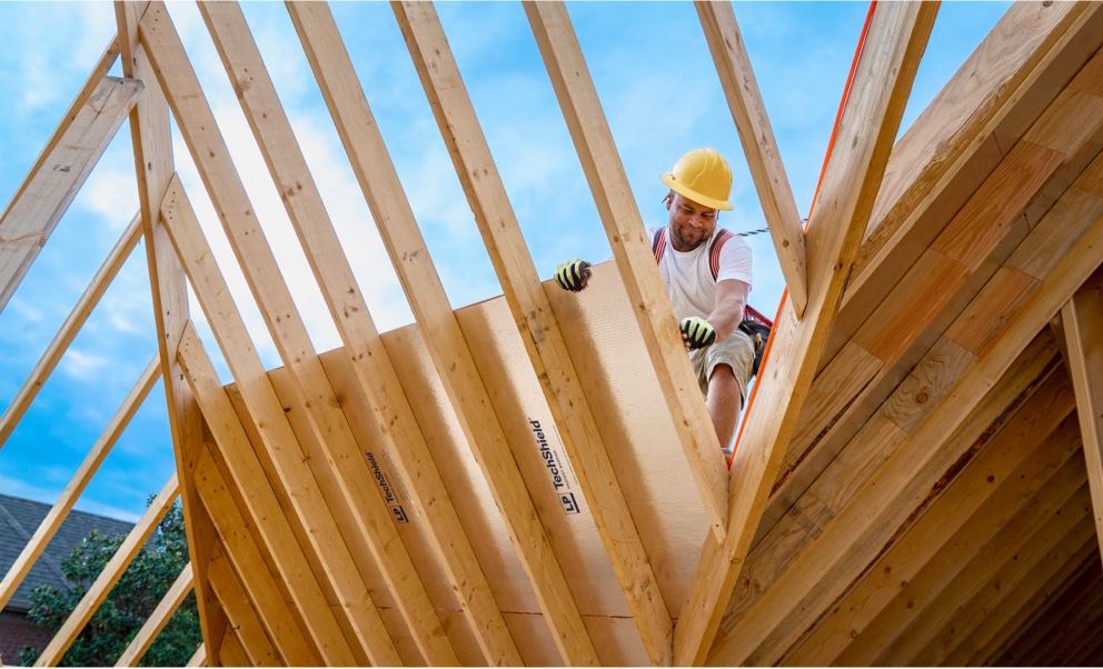 Un ouvrier sur une charpente de toit à forte pente, fixant une feuille de Techshield.